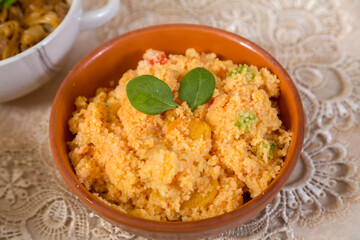 Couscous with dried fruits garnished with herbs in a clay plate on a tablecloth.