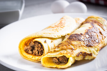 Delicious meat pancakes on a white plate, with eggs, wheat, olive oil, tomato sauce and checkered tablecloth in the background.