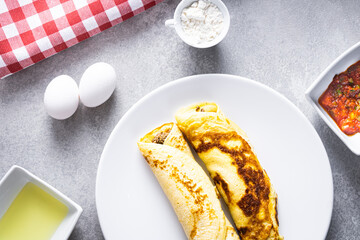 Delicious meat pancakes on a white plate, with eggs, wheat, olive oil, tomato sauce and checkered tablecloth in the background.