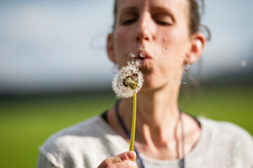 Young woman blowing dandelion bulb