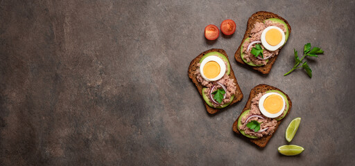 Obraz na płótnie Canvas Sandwiches with tuna, rye bread, boiled egg, avocado red onion on dark brown background. Top view, flat lay. Mediterranean food. Banner