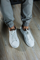 Men's summer shoes. Close-up of male legs in white leather sneakers. Collection of men's leather shoes
