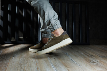 Close-up of male feet in green leather shoes. A young man is standing in leather stylish green sneakers in gray jeans. Summer men's shoes. Casual street style