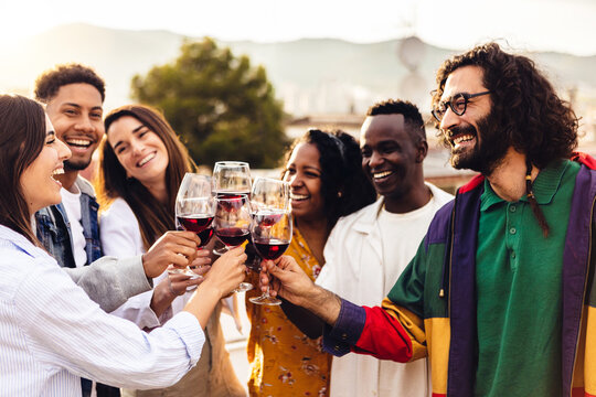 Happy group of young friends celebrating together cheering with red wine glasses at terrace summer party during sunset. Generative AI