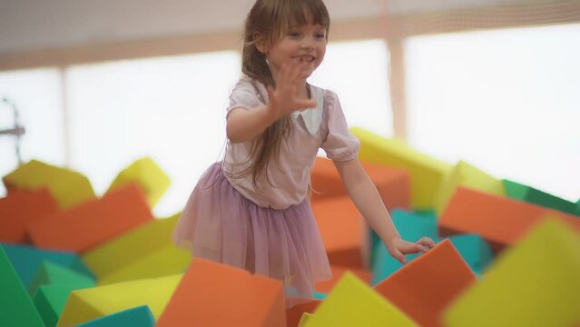 Little happy girl play and have fun in a dry pool with soft multicolored cubes in a children's entertainment center and throw ball in the playroom. Generative AI
