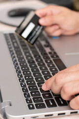 Vertical close up of hand typing in laptop and a hand holding a credit card in the bokeh background, online shopping concept