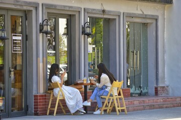 Obraz premium Two girls have breakfast in a summer street cafe in front of large mirrored cafe windows. Photos without faces and brands.