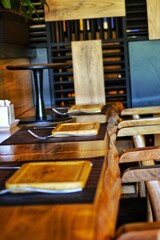 Wooden bar counter from a vertical saw cut of a tree. Loft cafe with warm lighting and brick wall. Serving with wooden utensils.