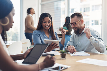 We did it. two business coworkers sitting together and celebrating an achievement together while their colleagues work around them.