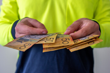 View of a tradesman in high visibility clothes holding australian dollar notes
