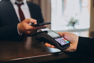 A businessman pays a bill for a hotel room through a smartphone using NFC technology.