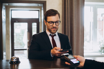 A businessman pays a bill for a hotel room through a smartphone using NFC technology.