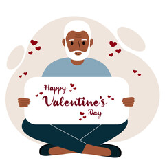 A man sits cross-legged and holds a large card with a congratulation for saint valentine.