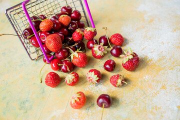 Fresh red fruit and berries in supermarket cart tray on yellow background. Copy space.tasty cherry...