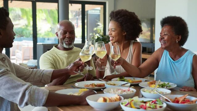 Family with senior parents and adult offspring around table at home doing cheers with wine before meal -shot in slow motion
