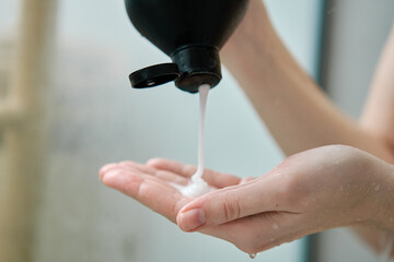 Pouring shampoo from bottle on female hand in bathroom. Hygiene concept