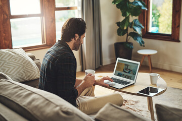 Let the blogging begin. a handsome young man using his laptop while relaxing on a couch at home.