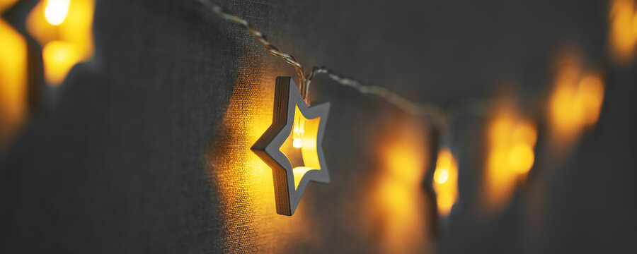 Holiday lights in stars shape hanging on string at grey wallpaper background. Christmas home decoration concept.
