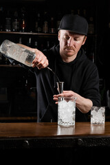 Bartender prepares traditional Negroni cocktail at the bar. Bartender mixes gin, campari, and sweet vermouth to prepare the Negroni alcoholic cocktail.