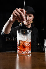 Bartender mixes gin, campari, and sweet vermouth to prepare the Negroni alcoholic cocktail. Bartender prepares traditional Negroni cocktail at the bar.