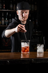 Bartender mixes gin, campari, and sweet vermouth to prepare the Negroni alcoholic cocktail. Bartender prepares traditional Negroni cocktail at the bar.