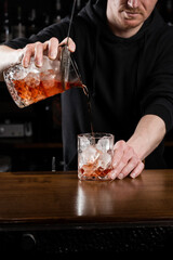 Bartender pours mixed traditional Negroni cocktail in the glass at the bar. Bartender mixes gin, campari, and sweet vermouth to prepare the Negroni alcoholic cocktail.