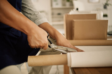 Closeup of tailor cutting fabric at his table. Hands of fashion designer cutting material. Seamstress cutting textiles with a scissor. Small business owner working in a design studio