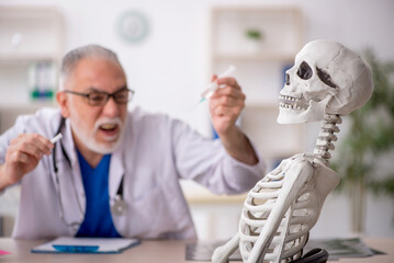 Old male doctor examining skeleton in the clinic