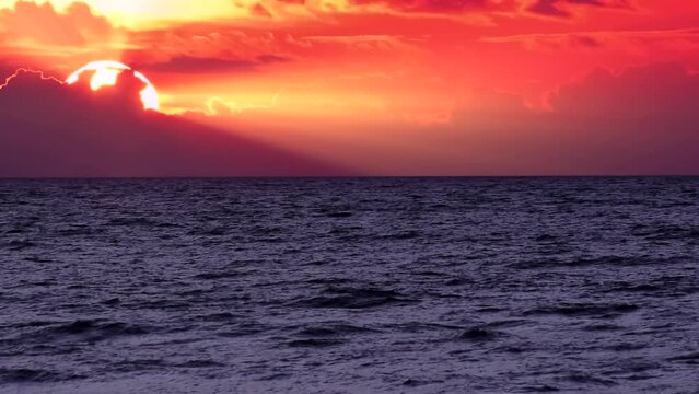 Sea waves on the red and orange colour sunset background. Beautiful sunrays with clouds on the sky, calm horizon scene by the beach, close up, slow motion, panning hd. ProRes 422 HQ.