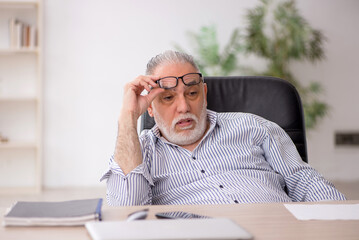 Naklejka premium Old male employee working in the office