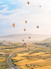 Flying in sky many bright colored beautiful balloons into air in Cappadocia in mountains early at sunrise, dawn. Filling balloon with hot air from burner, big basket. Tourists excursion, cloud flight