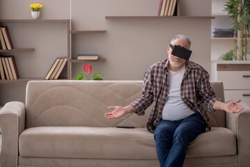 Obraz premium Old man wearing virtual glasses at home