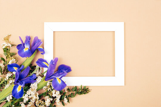 Blank picture frame and bouquet of blue iris flowers on beige background. Holiday concept. Top view, flat lay, mockup