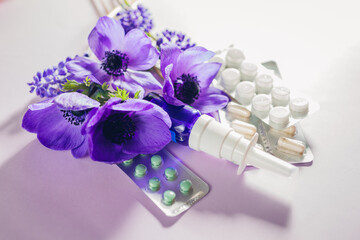 Seasonal spring allergy background. Pills and nasal spray flat lay with purple flowers. Pollen...