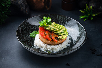Dinner pork cutlet with rice, avocado, tomatoes, greens and spices.