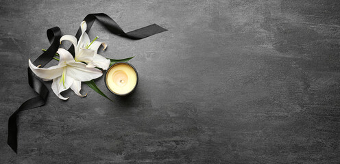 Burning candle, white lily flowers and black funeral ribbon on dark background with space for text