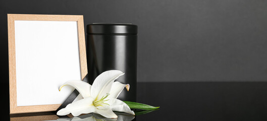 Mortuary urn, blank photo frame and white lily flower on dark background with space for text