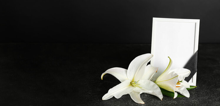 Blank funeral frame and beautiful lily flowers on dark background with space for text