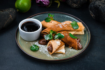 Sweet thin pancakes with chocolate paste, mint and sauce.