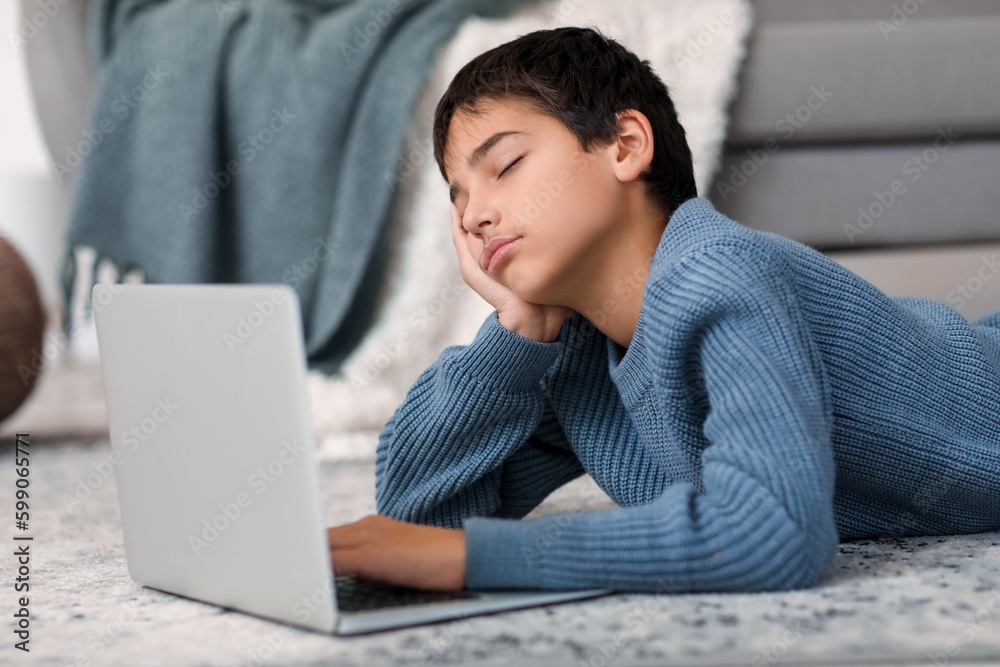 Poster Tired little boy sleeping near laptop on floor at home