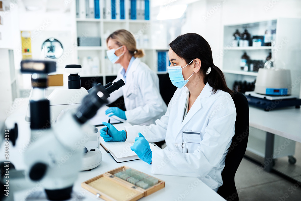 Poster Getting stuck right in to some lab work. a young scientist working in a lab with her colleague in the background.