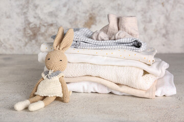 Stack of baby clothes and knitted toy bunny on light background