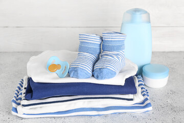 Stack of baby clothes, pacifier and cosmetics on table