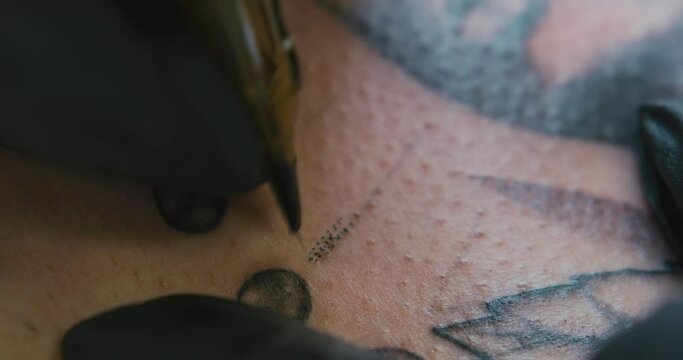 Extreme close-up of the needle of a tattoo machine in the hands of a tattoo artist making straight lines using the dotwork technique