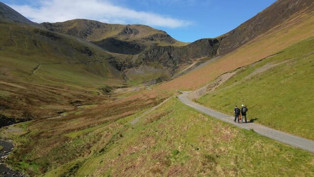 Hikers walking into valley along track on sunny day at Coledale Beck in the English Lake District Cumbria