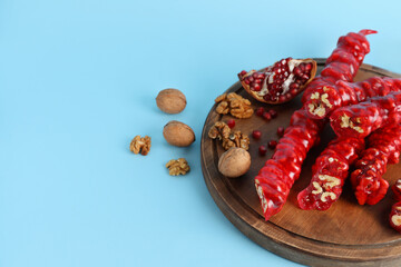 Wooden board with tasty churchkhela, walnuts and pomegranate on color background