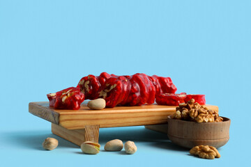 Wooden boARD WITH tasty churchkhela and nuts on color background