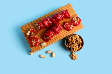 Wooden boARD WITH tasty churchkhela and nuts on color background