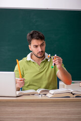 Young male student physicist in front of green board