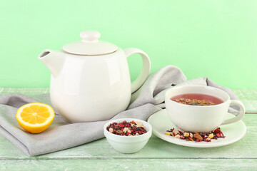 Cup of fruit tea, teapot and lemon on green wooden table